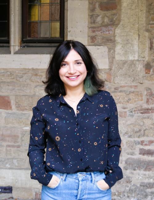 Camli Badrya stands with hands in pockets against a brick background